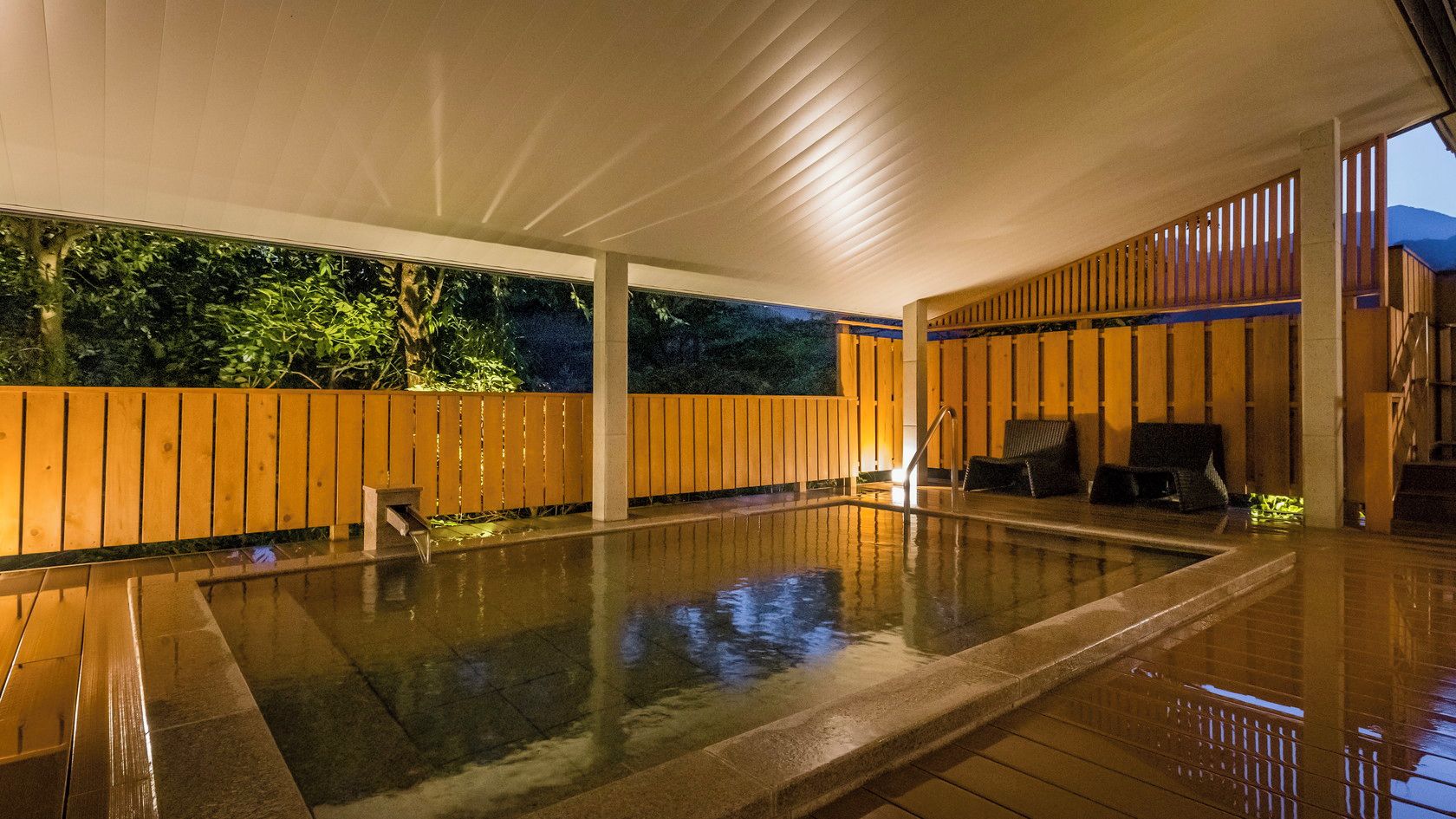 A covered outdoor swimming pool with a wooden deck and seating area.