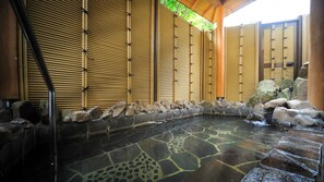 Un espace de sources chaudes doté d’un sol en pierre, de cloisons en bambou et d’un mur en pierre agrémenté de rochers.