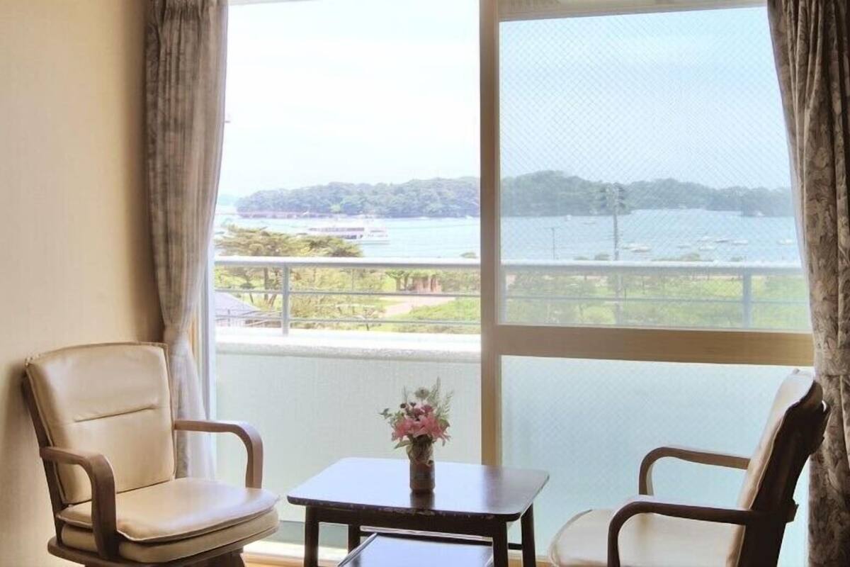 A room with two chairs, a small table, and a view of a body of water and greenery.