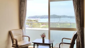 Ein Zimmer mit zwei Stühlen, einem kleinen Tisch und Blick auf ein Gewässer und Grünflächen.