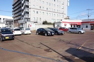 Un estacionamiento con varios autos, un edificio con balcones y una panadería con toldo rojo.