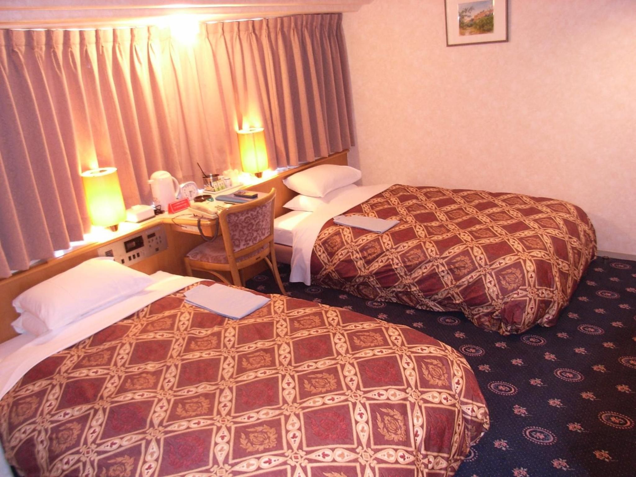 Une chambre d’hôtel avec deux lits, un bureau avec une chaise, une lampe et une horloge.