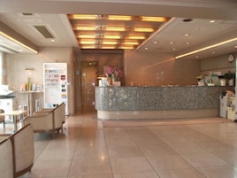 Zona de recepción de un hotel con mostrador de mármol, asientos y un reloj en la pared.