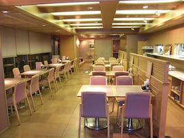 Un comedor de hotel con varias mesas y sillas, una zona de cocina y un mostrador de recepción.