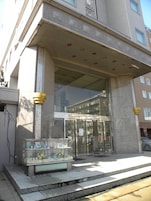 Entrada de un edificio con puerta de vidrio y una pequeña vitrina con objetos.