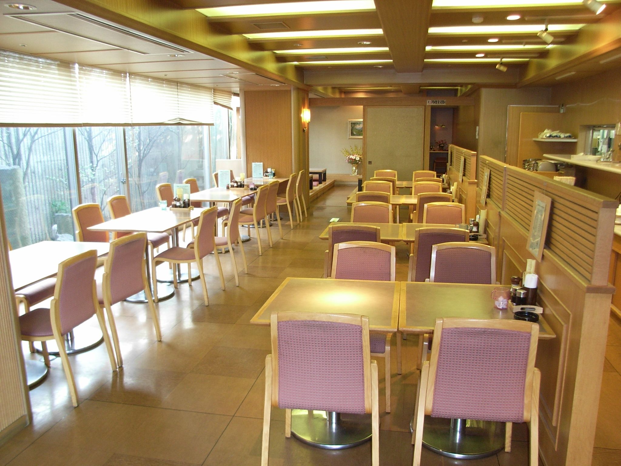 A restaurant with multiple tables and chairs, a counter, and a view through large windows.