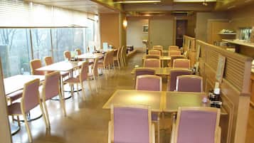 A restaurant with multiple tables and chairs, a counter, and a view through large windows.