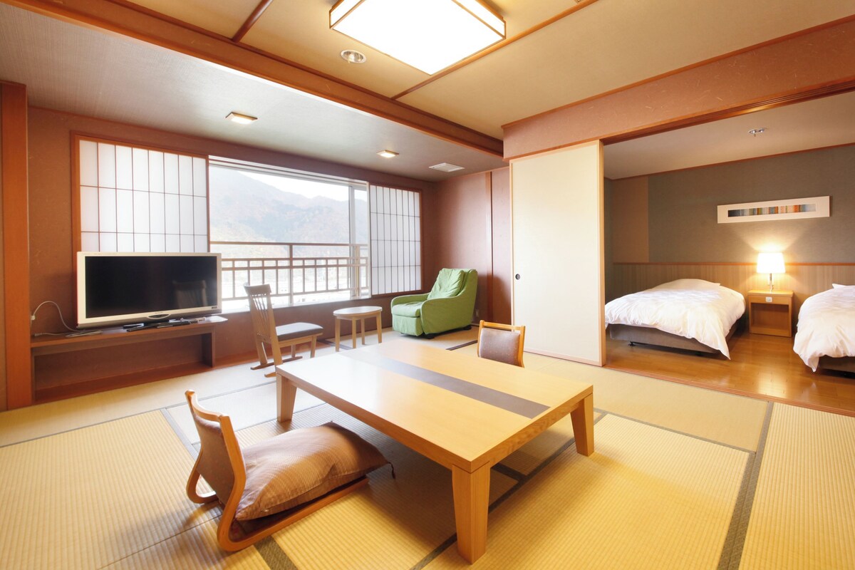Een traditionele Japanse kamer met tatami vloerbedekking, een lage tafel, een televisie en twee bedden.