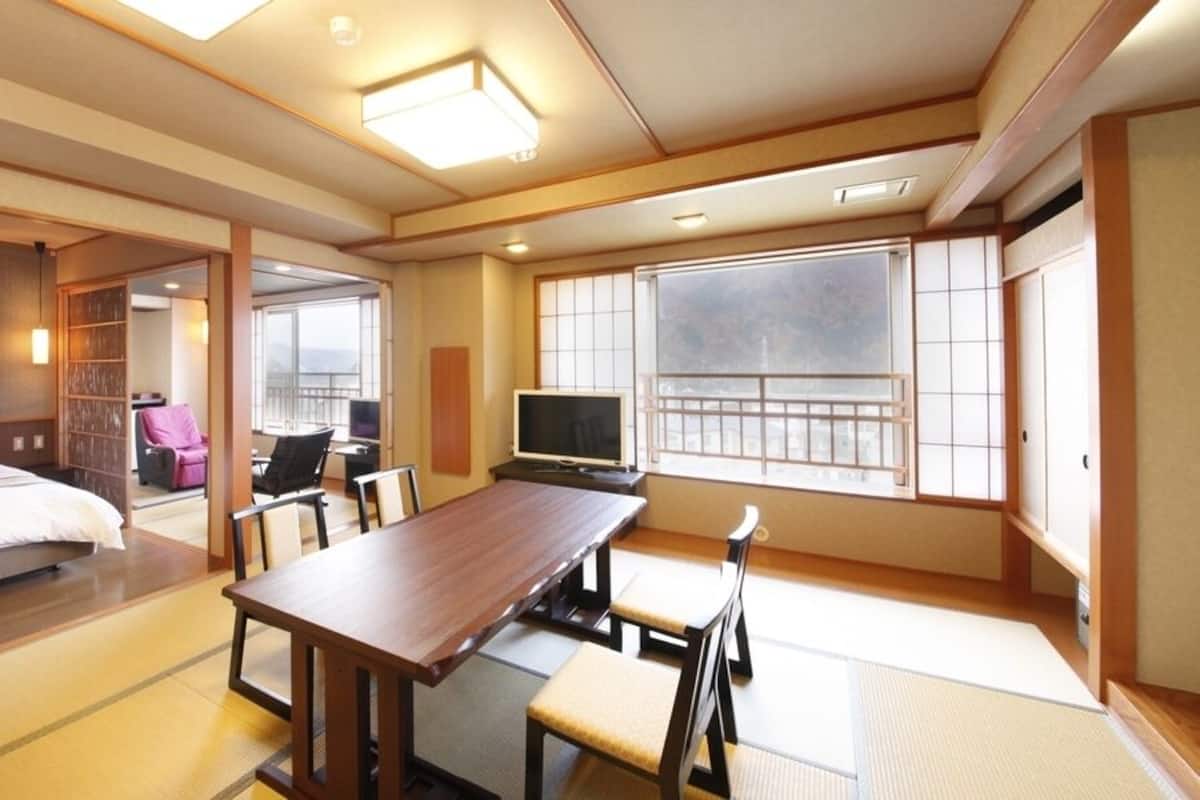 Ein traditioneller japanischer Raum mit Tatami-Bodenbelag, einem Bett, einem Fernseher und einem Balkon mit Blick.