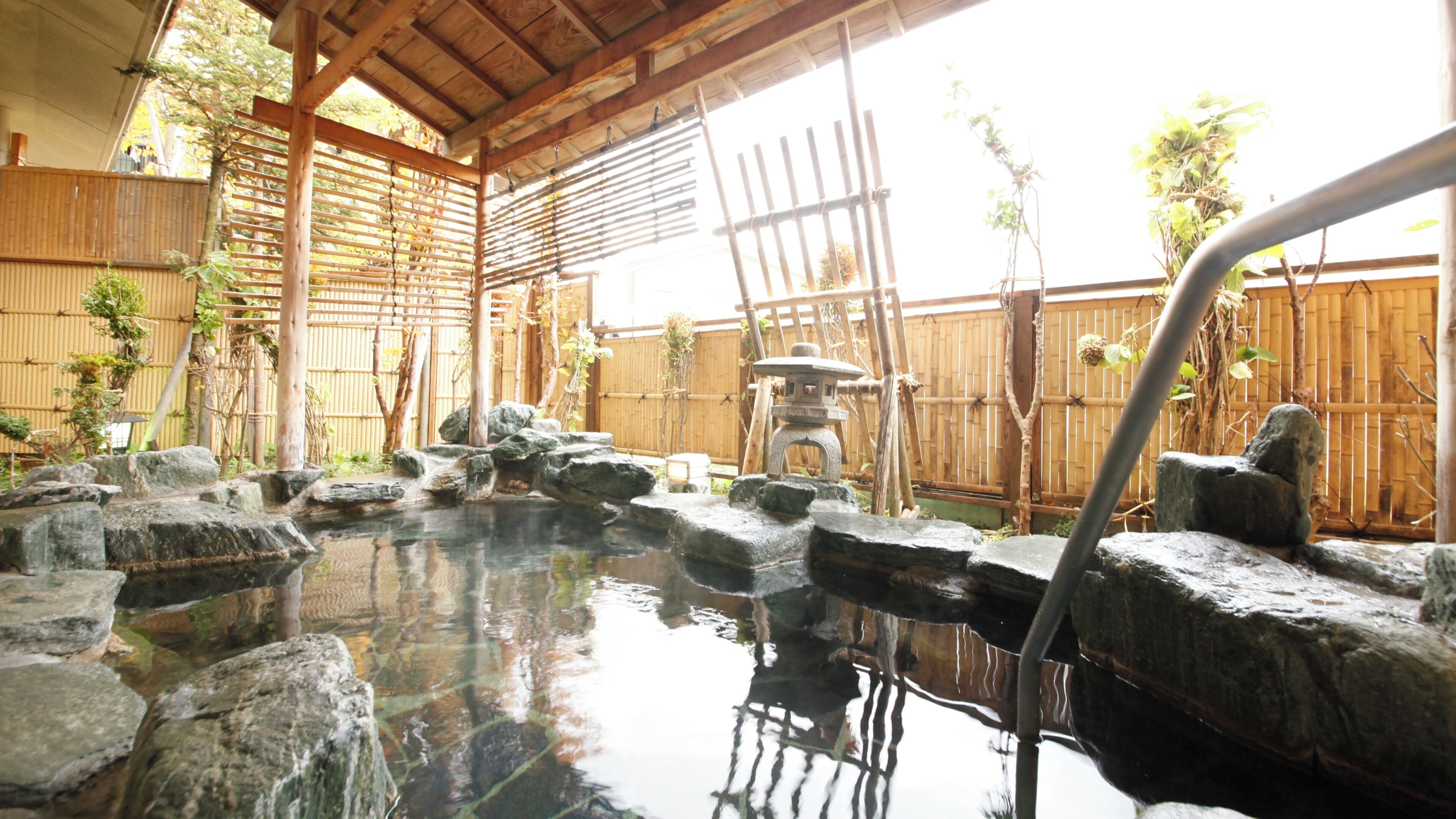 A traditional Japanese garden with a stone hot spring, bamboo fences, and a wooden structure.