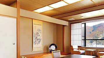 Un salón de conferencias con una larga mesa, sillas, un amplio ventanal con vistas a un paisaje montañoso y una obra de arte tradicional japonesa en la pared.