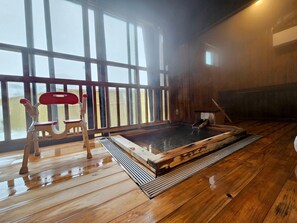 A wooden interior with a hot tub, a wooden bench, and a window with a view.