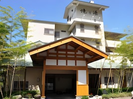 Un edificio japonés tradicional con una estructura de entrada de madera, un edificio de varios pisos al fondo y follaje circundante.