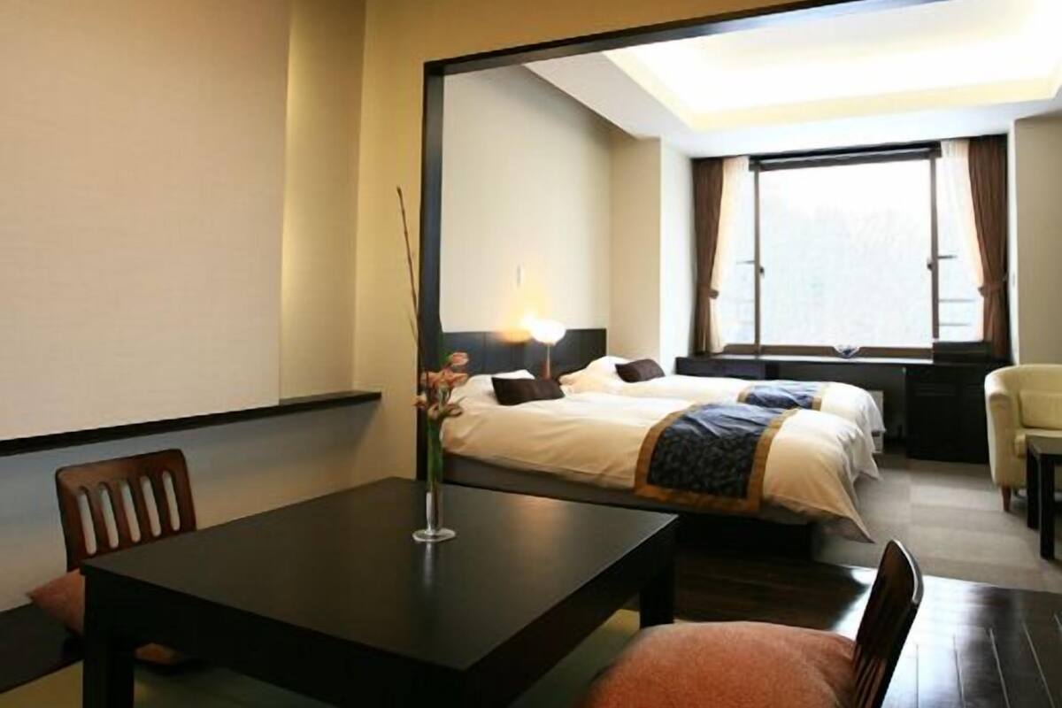 A hotel room with a dining table, two beds, a chair, and a large mirror.