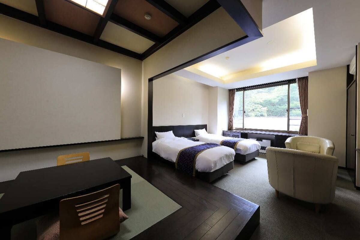A hotel room with a large bed, a smaller bed, a desk, a chair, and a large window.