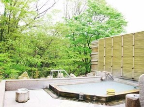 Ett traditionellt japanskt onsen med ett stenbad, omgivet av frodig grönska och ett bambustaket.
