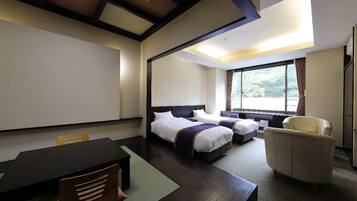 A hotel room with a large bed, a smaller bed, a desk, a chair, and a large window with curtains.