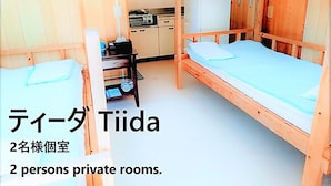 Een kamer met twee houten bedden, een klein tafeltje en een televisie. Het is aangeduid als een privékamer voor twee personen.