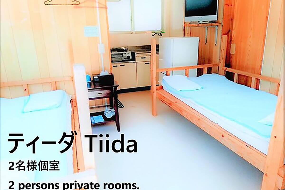 Een kamer met twee houten bedden, een klein tafeltje en een televisie. Het is aangeduid als een privékamer voor twee personen.