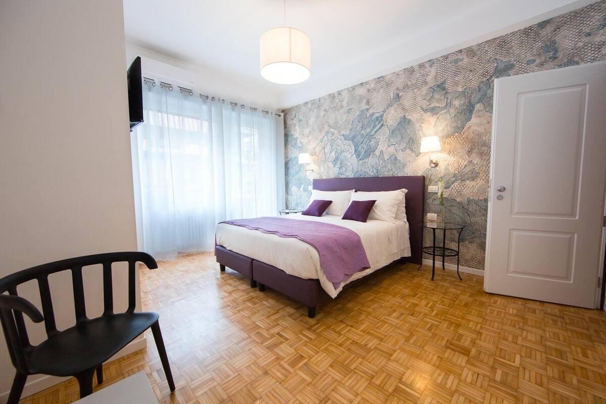 A bedroom with a bed, a chair, a lamp, and a door.