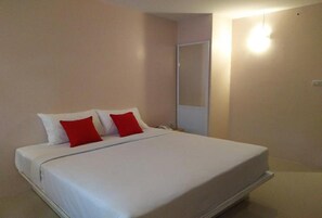 A single bed with white bedding and two red pillows in a room with beige walls and a door. - Bird Room Hotel (Bangkok)