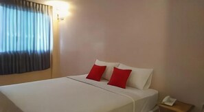 A hotel room with a bed, two red pillows, a bedside table with a phone, and a window with curtains. - Bird Room Hotel (Bangkok)