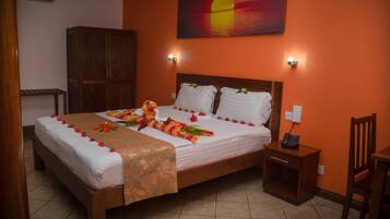 A hotel room with a bed, a nightstand, a wooden wardrobe, and a painting of a sunset.