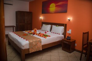 Quarto de hotel com cama, mesa de cabeceira, guarda-roupa de madeira e uma pintura de pôr do sol.