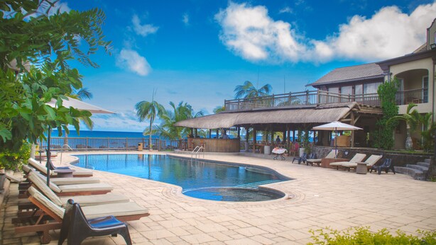 Ein Poolbereich mit Liegestühlen, Sonnenschirmen und Blick aufs Meer.