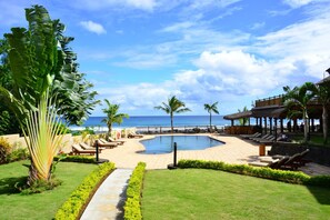 Área da piscina com espreguiçadeiras e vista para o oceano.