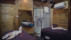 Eine Holzhütte mit zwei Betten, einem Badezimmer mit Waschbecken und Dusche sowie einer Klimaanlage.