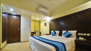 A hotel room with a large bed, a bedside table with a phone, a wall-mounted air conditioner, and a door. - Azurra Hotels (New Delhi)