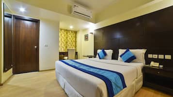 A hotel room with a large bed, a bedside table with a phone, a wall-mounted air conditioner, and a door.