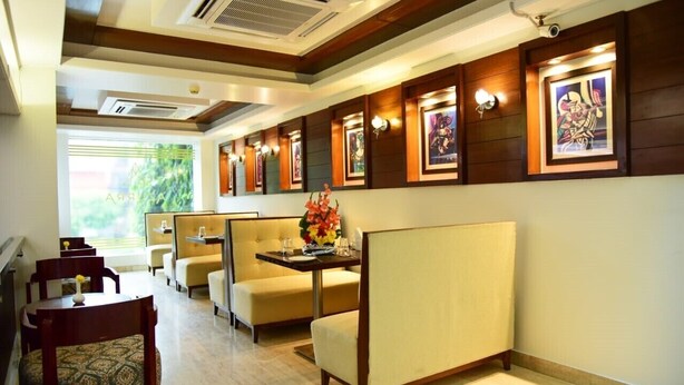 A hotel lobby with seating areas, framed artwork on the walls, and a view of greenery outside. - Azurra Hotels (New Delhi)
