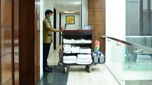 A hotel lobby with a wooden reception desk, a cart with folded towels, and a glass railing overlooking the interior. - Azurra Hotels (New Delhi)