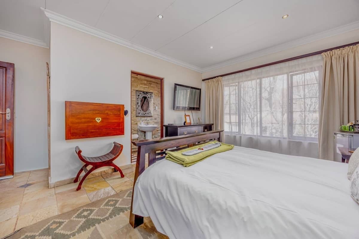 Una camera d'albergo con un letto, una scrivania, una sedia, una televisione e una finestra con tende.