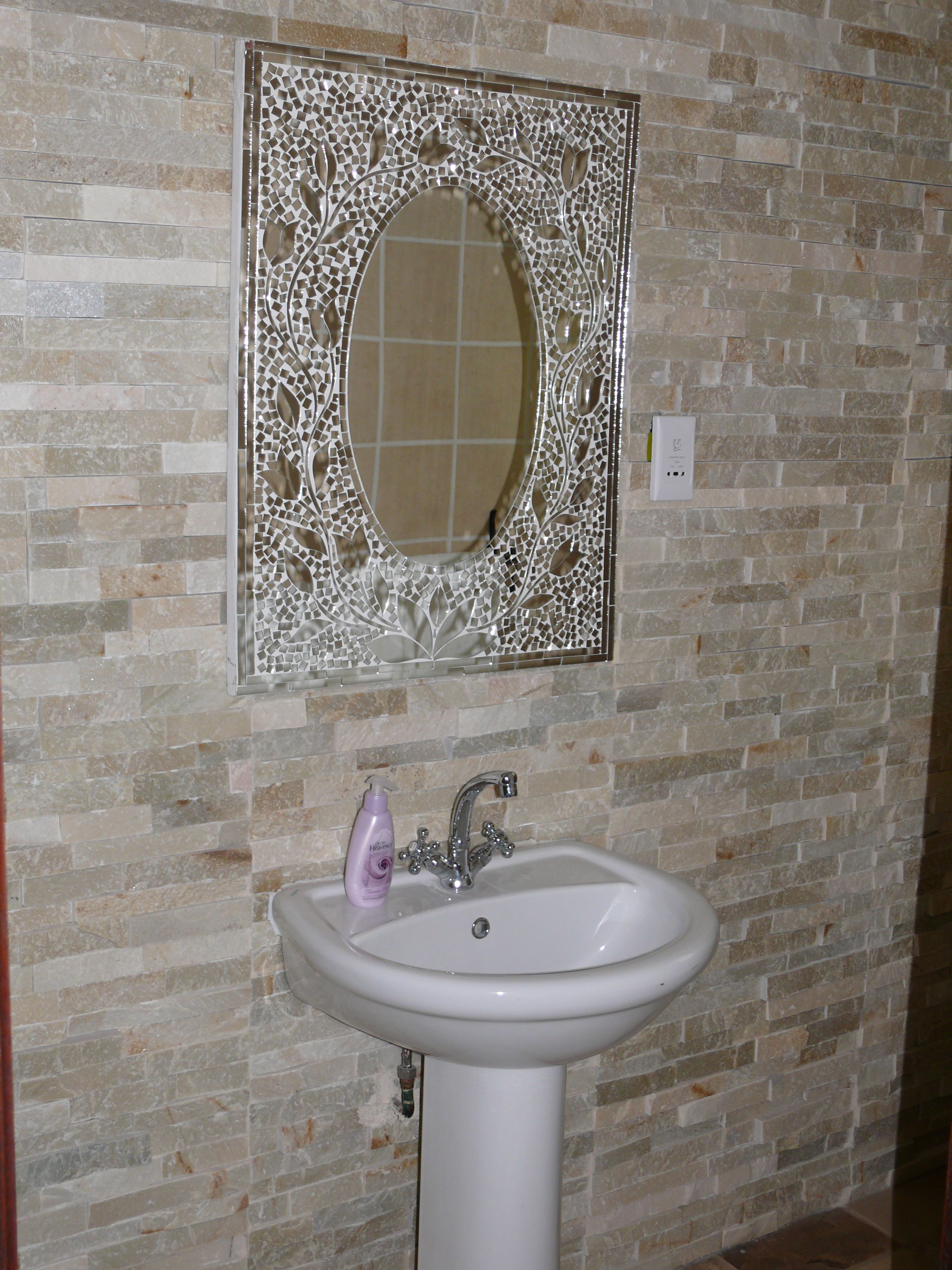 A bathroom with a mosaic tile wall, a white sink with a single faucet, and a mirror with a decorative frame.