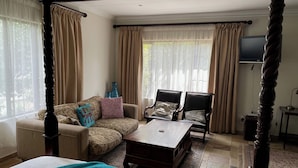 A four-poster bed, a sofa, two armchairs, a coffee table, and a television in a well-lit room with large windows and curtains. - 42onKing (Centurion)