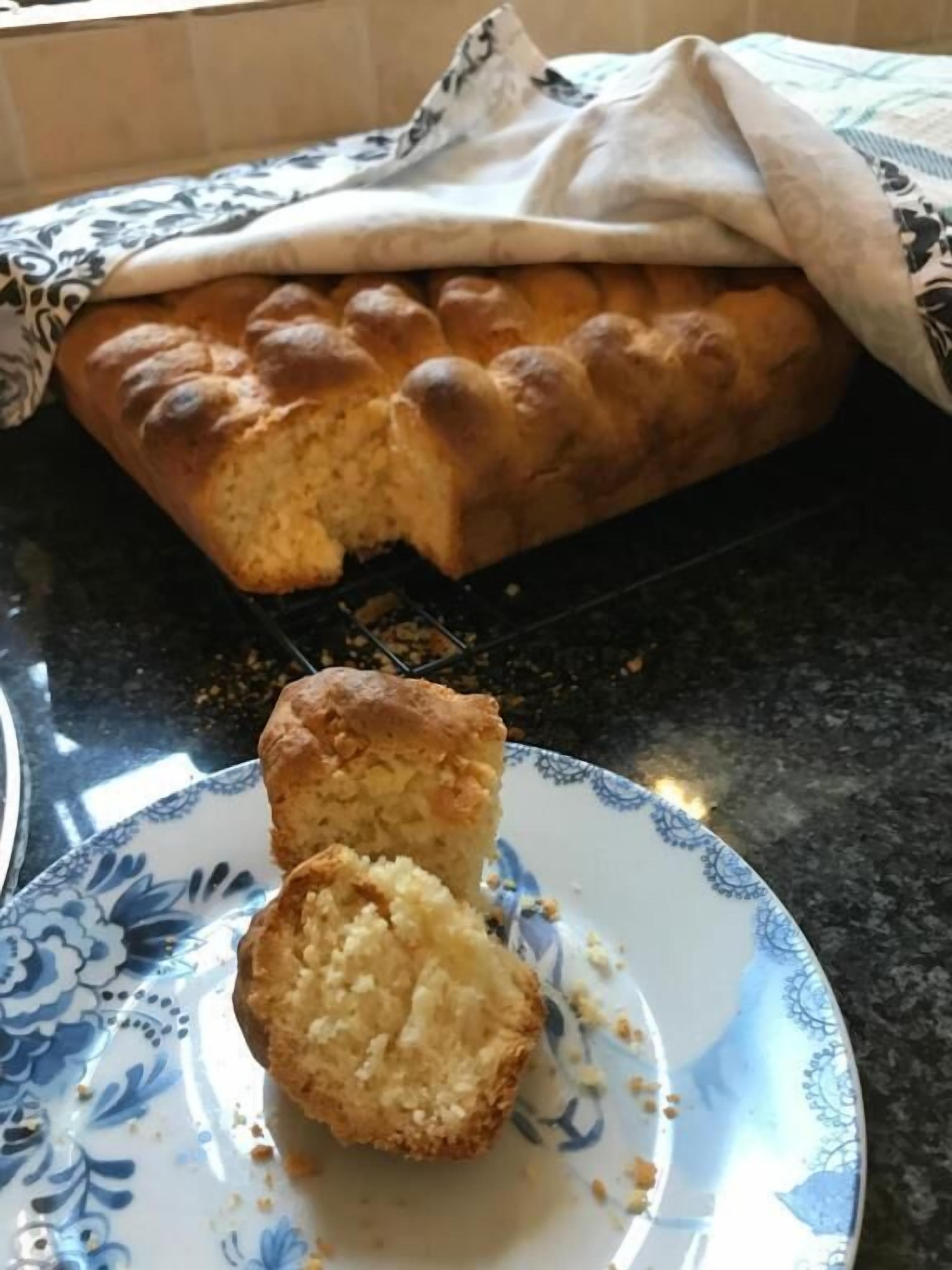 A loaf of bread on a cooling rack and two muffins on a plate.