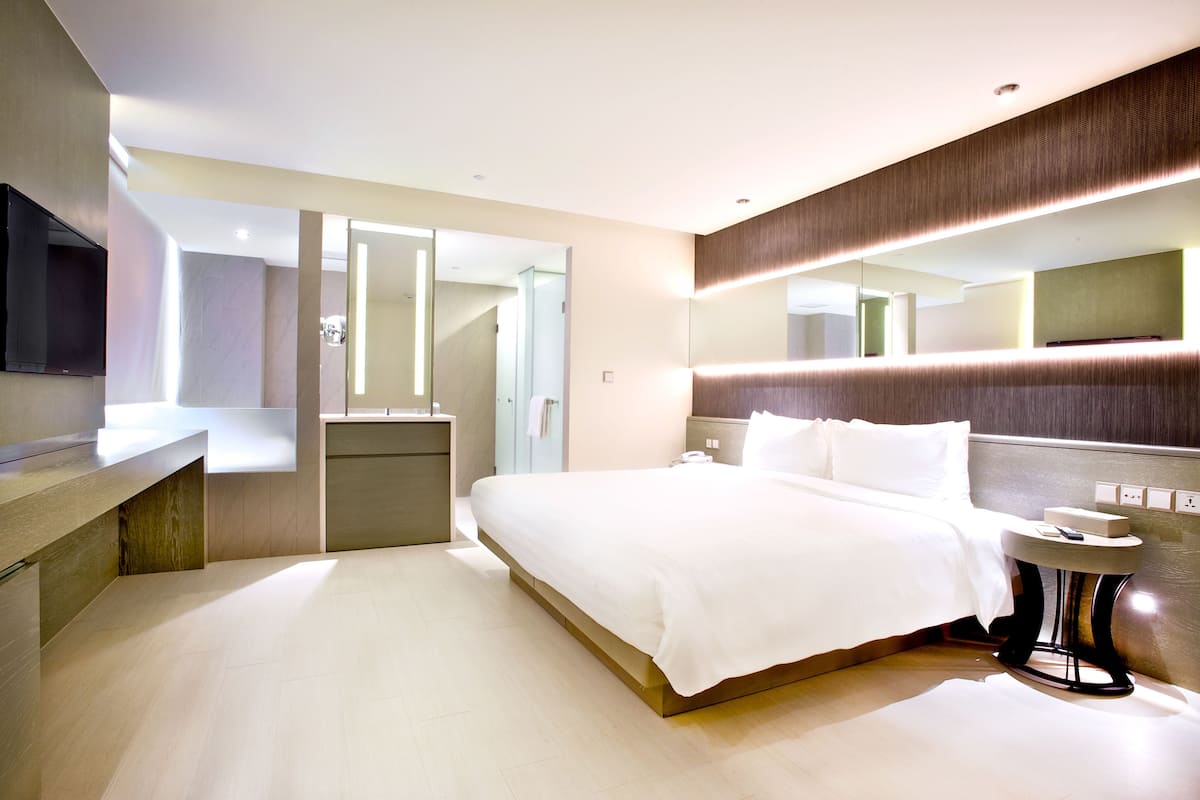 Une chambre d’hôtel moderne dotée d’un grand lit, de tables de chevet, d’un téléviseur à écran plat et d’un miroir.