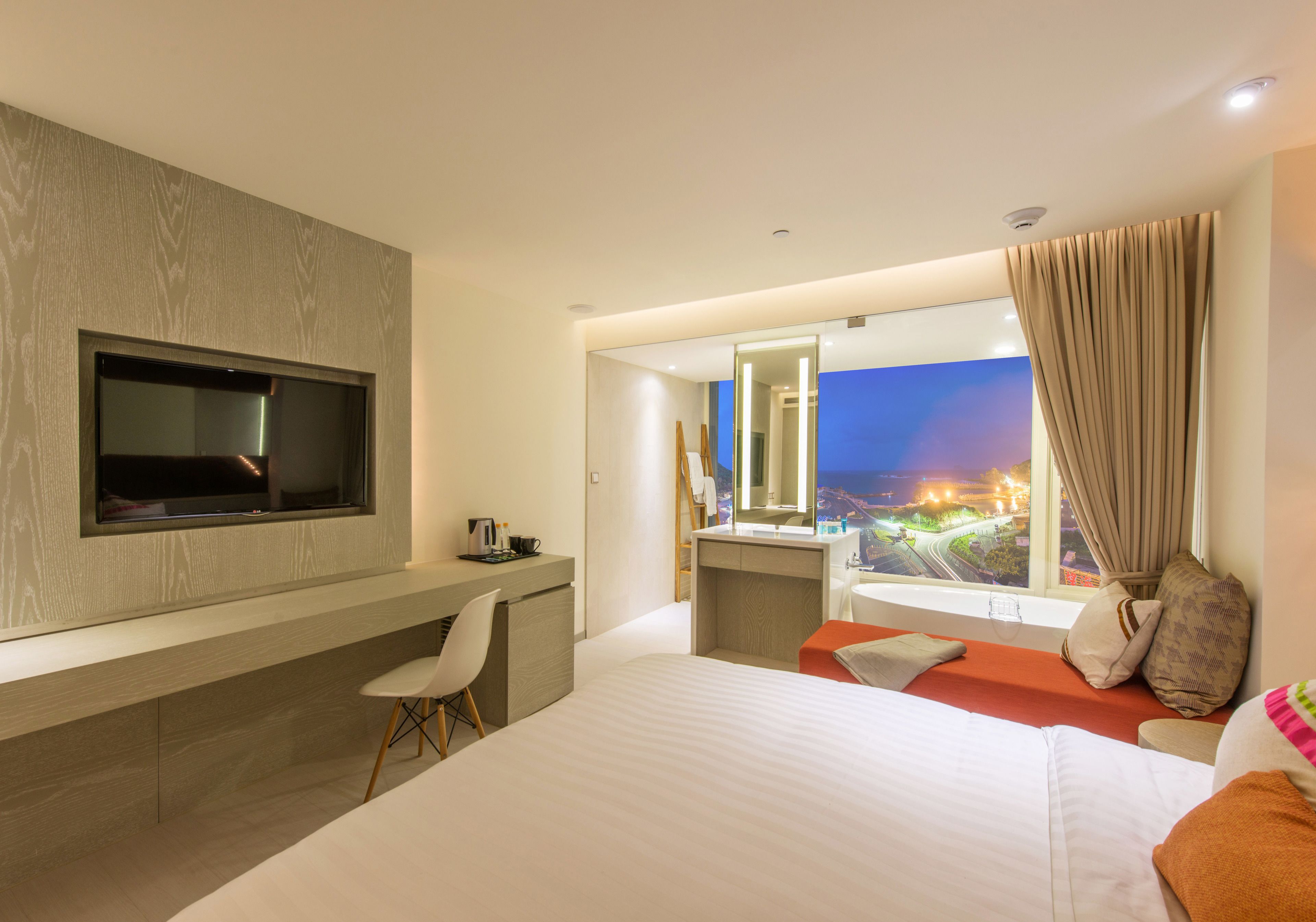 Une chambre d’hôtel moderne dotée d’un grand lit, d’un bureau, d’une télévision, d’une salle de bain et offrant une vue sur la ville la nuit.