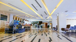 Een moderne hotel lobby met een gepolijste marmeren vloer, een receptiebalie en een trap naar de verdiepingen erboven.