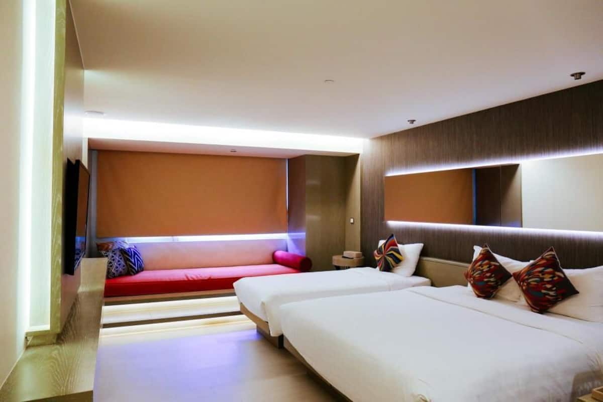 Une chambre d’hôtel moderne avec deux lits, un canapé rouge et un grand miroir.