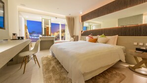 Een moderne hotelkamer met een groot bed, een bureau en uitzicht op een stadsbeeld in de schemering.