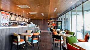 Een modern café met houten plafond, grote ramen en kleurrijke stoelen.