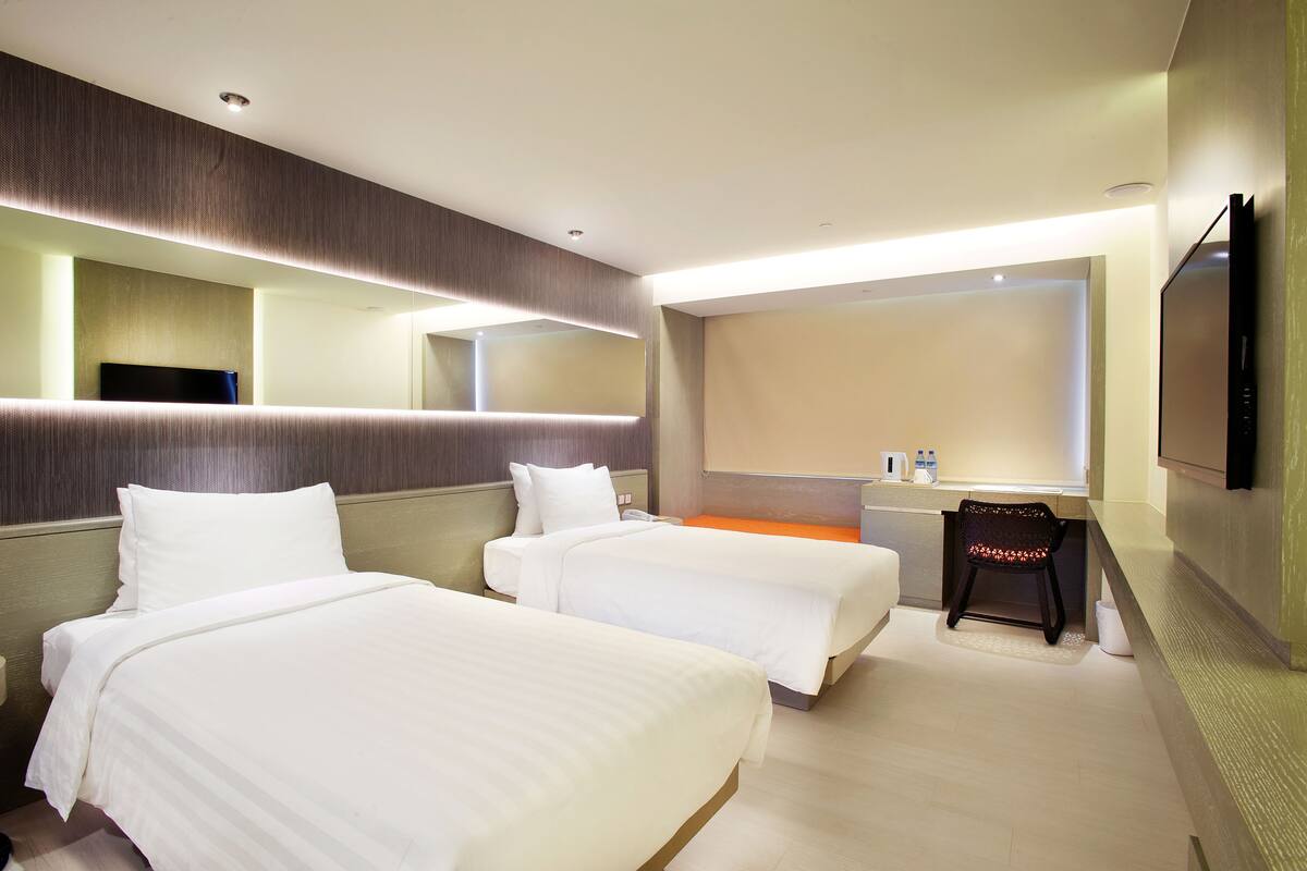 Une chambre d’hôtel avec deux lits, une petite table avec une chaise, une télévision et un grand miroir.