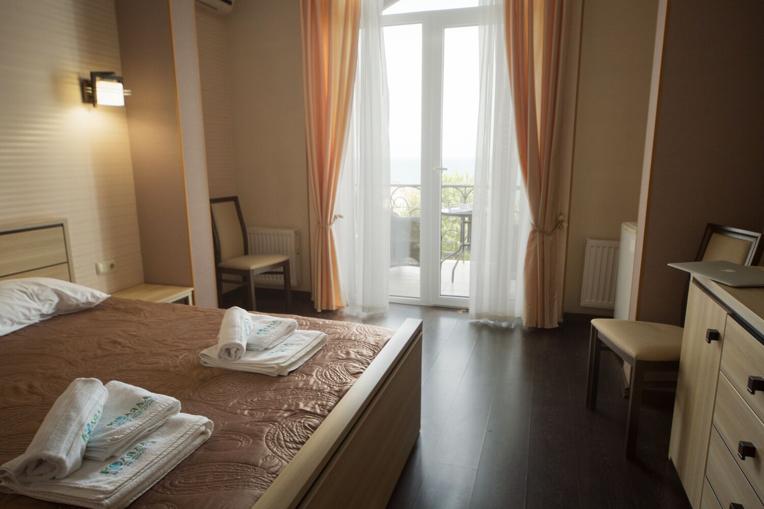 A hotel room with a bed, a desk, a chair, and a view of the outdoors through a glass door.