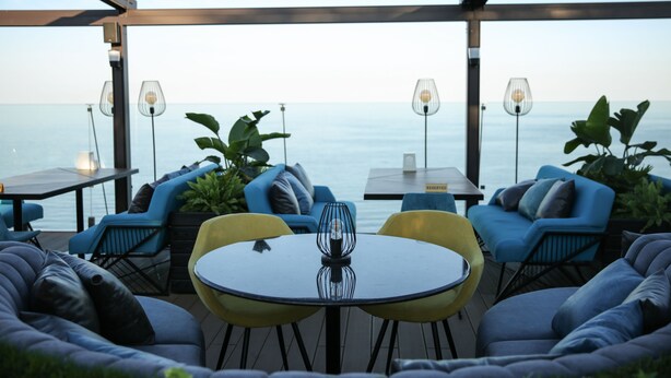 An outdoor seating area with a table and chairs, overlooking a body of water. - Hotel Kolyda (Sovinion)