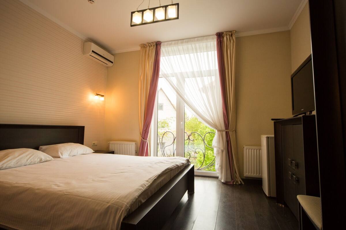 A hotel room with a large bed, a television, and a window with curtains.