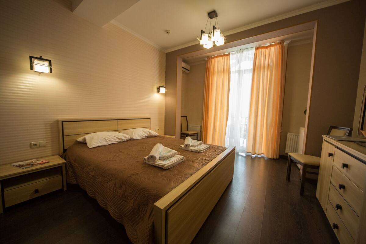 A bedroom with a large bed, bedside tables, a dresser, a chair, and a window with curtains.